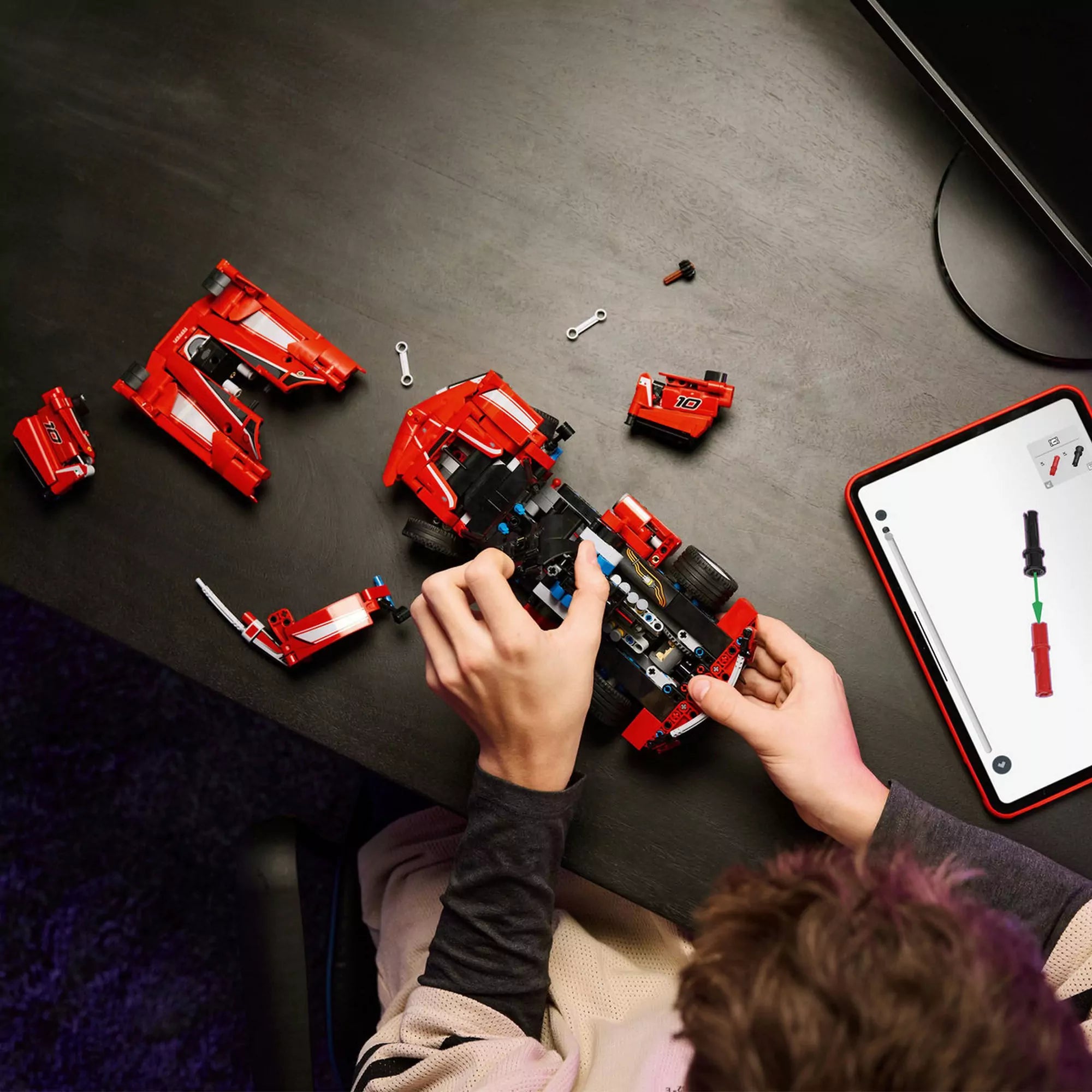 LEGO Technic Ferrari FXX K (42212) építés közben – Egy gyerek a versenyautó darabjait szereli össze tableten futó útmutató segítségével.