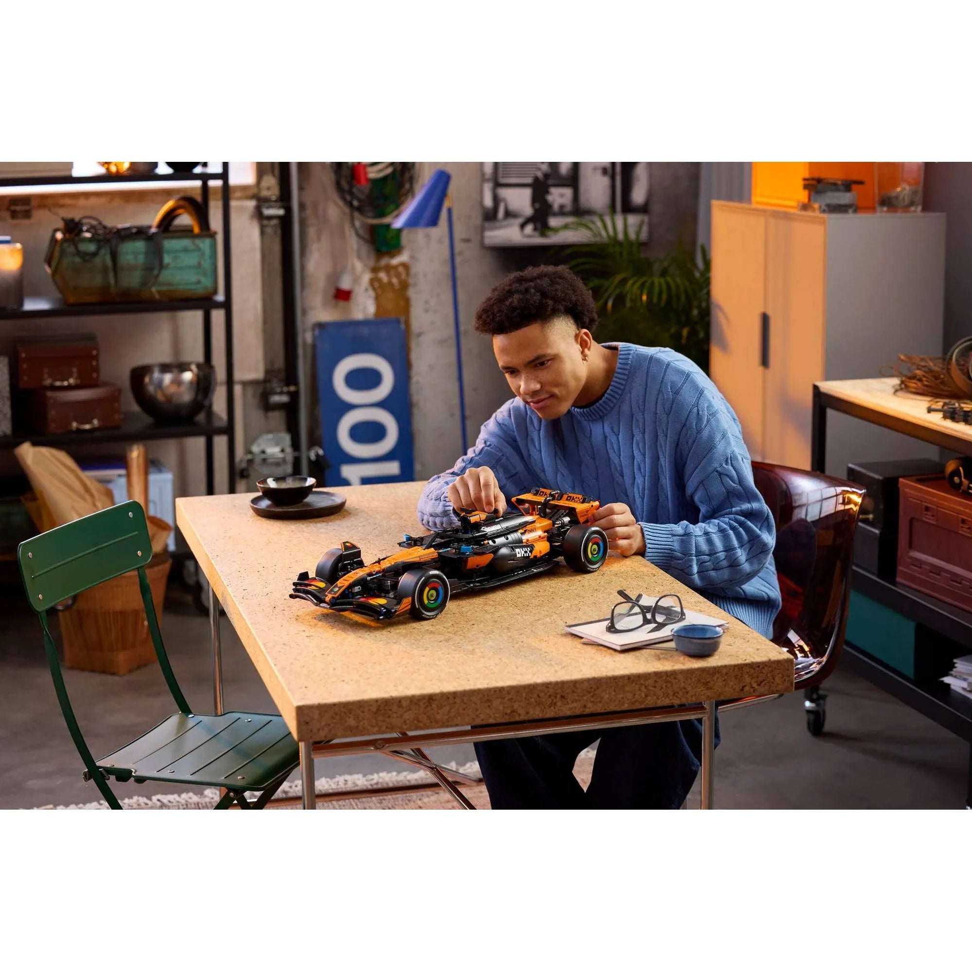 Felnőtt építi a LEGO Technic McLaren MCL39 F1 autó (42228) készletet egy asztalon, a megépített modell és alkatrészek társaságában.