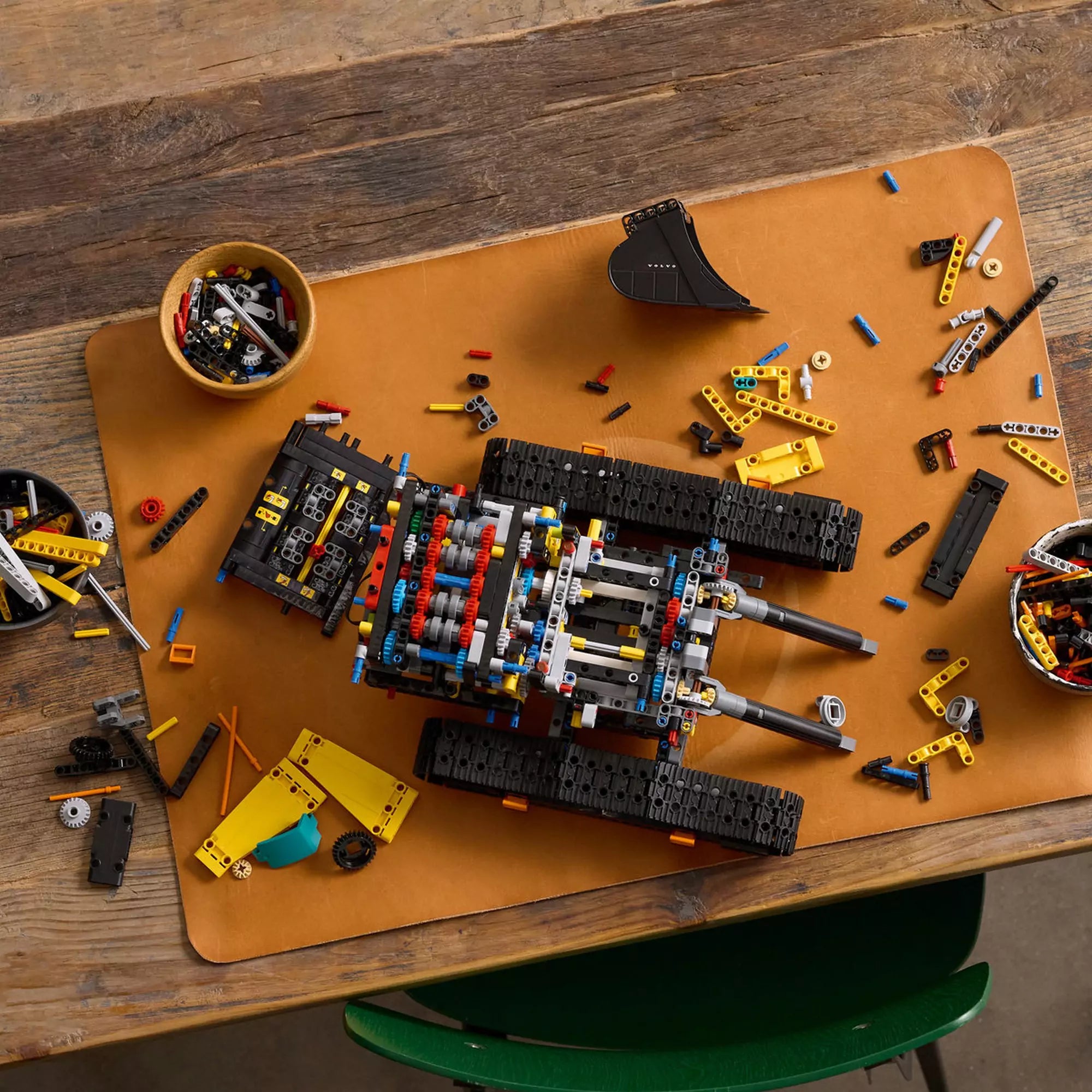 LEGO Technic Volvo EC500 Hybrid exkavátor (42215) építés közben – Az exkavátor váza és lánctalpa részletezve, szétszórt LEGO elemekkel asztalon.
