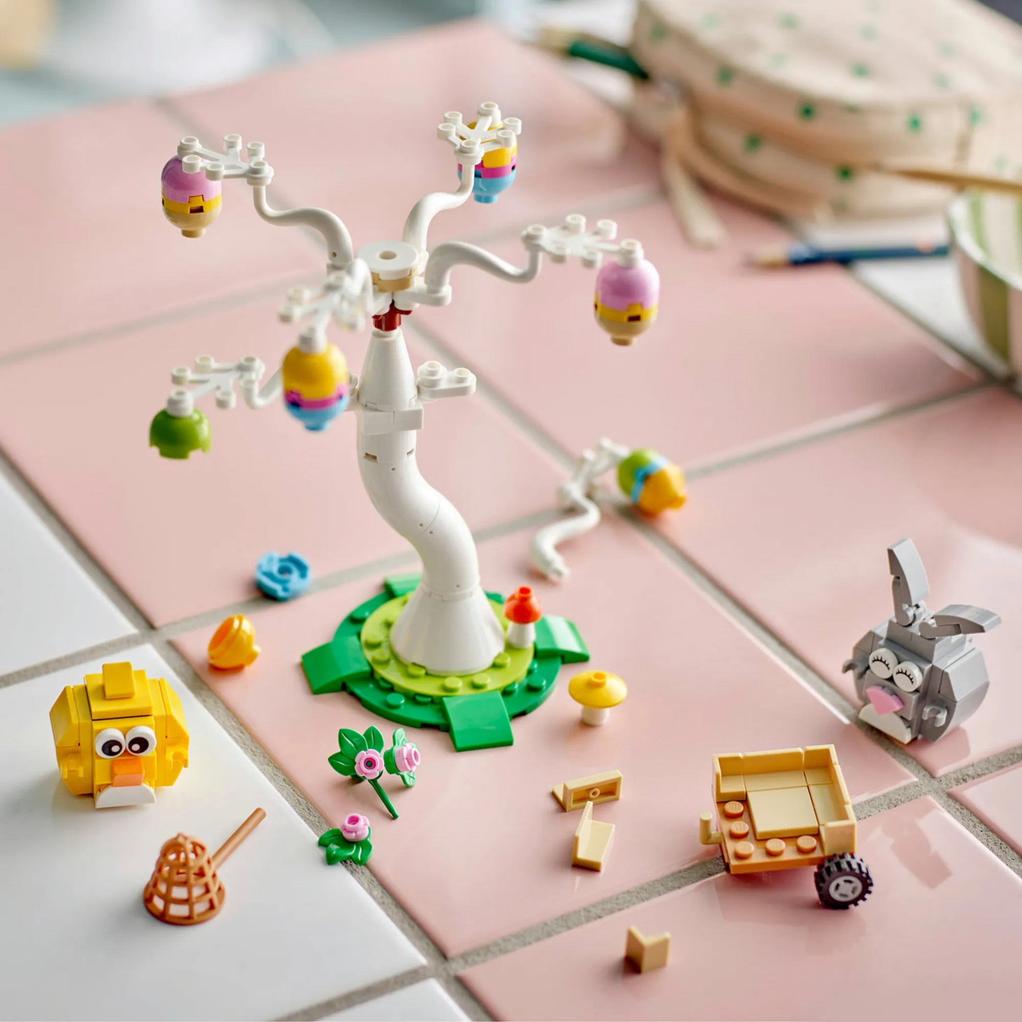LEGO Tojásvadászat nyuszival és csibével 40808 – Szétszedett és építés közbeni jelenet a tojásfával, figurákkal és kiegészítőkkel rózsaszín felületen.