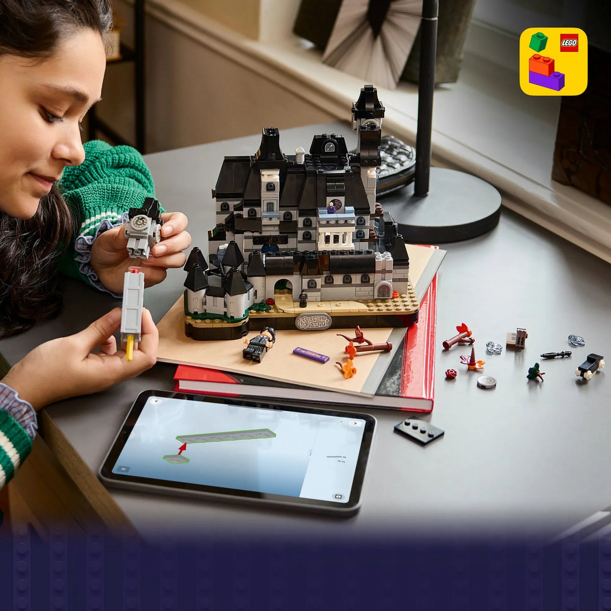 Egy lány a LEGO Wednesday: Nevermore Akadémia 76788 óratornyát építi, előtte tableten megjelenített építési útmutatóval.