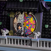 „A LEGO Wednesday & Enid’s Dorm Room készlet felépített modellje polcra helyezve: a sötét tetőszerkezet, a pókhálós ablak, az erkély gargoyle díszei és a két minifigura jól látható a gótikus épületen.”