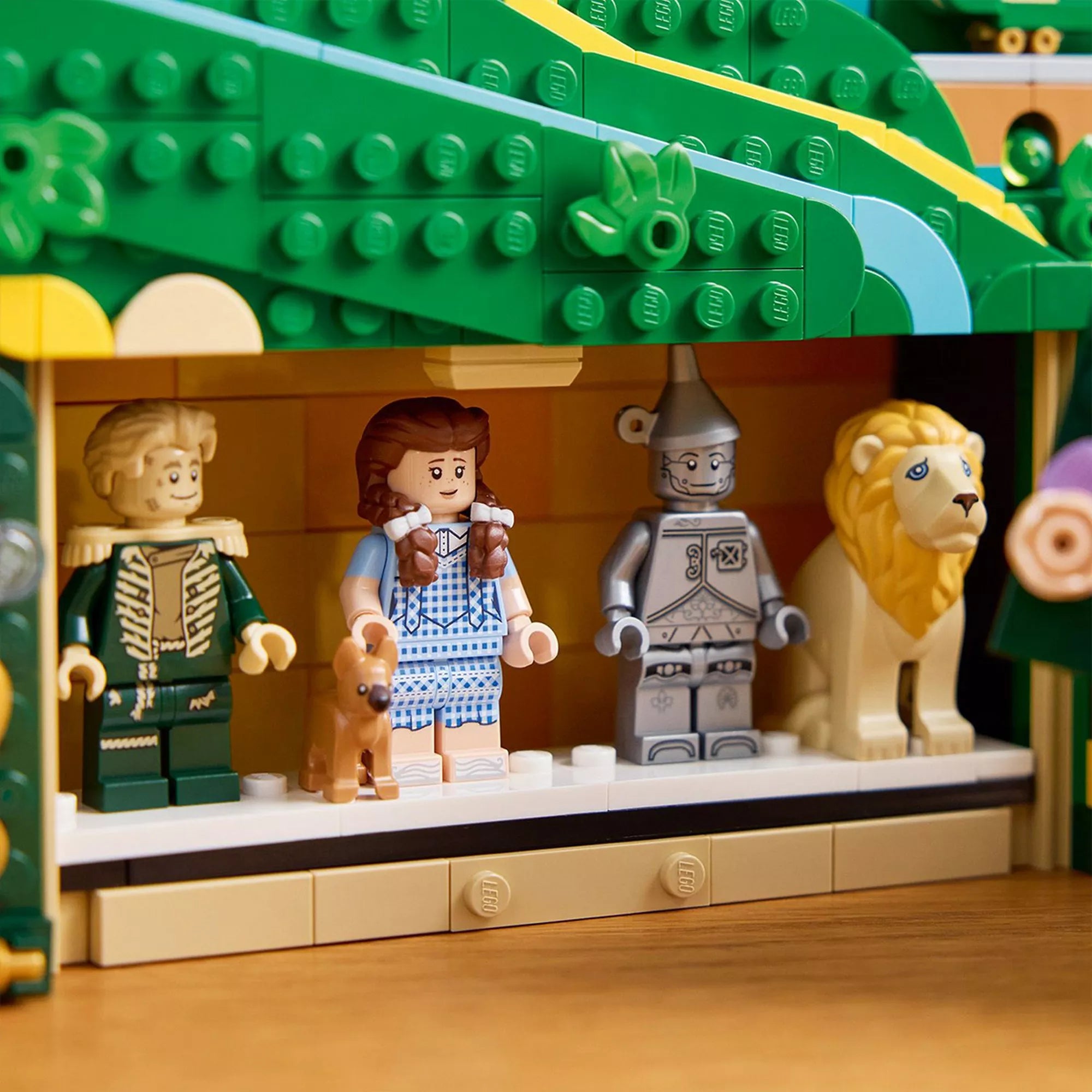 Közelkép a LEGO Wicked készlet titkos rekeszéről, amelyben a négy ikonikus minifigura – Dorothy, Toto, Bádogember és Oroszlán – áll egymás mellett egy rejtett polcon. A jelenet részletesen megmutatja a figurák ruházatát és arcvonásait.