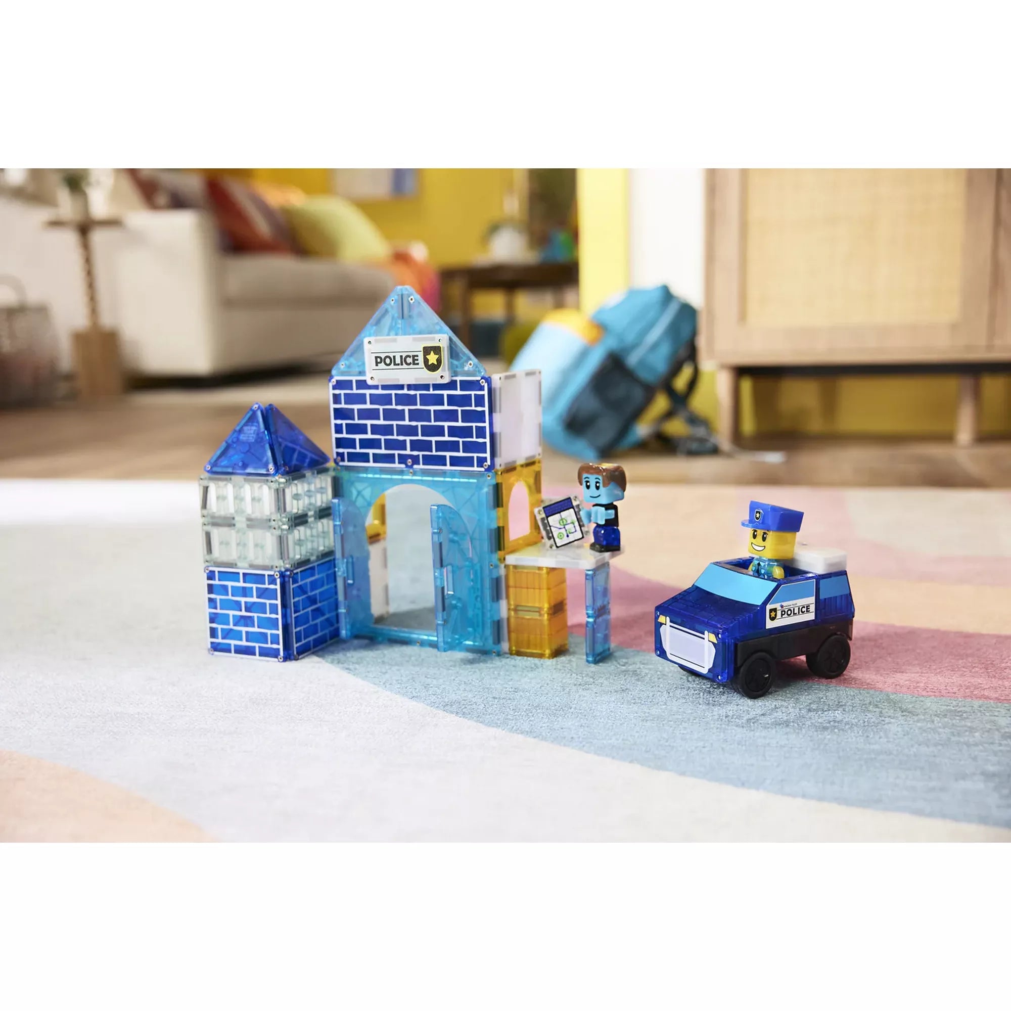A MAGNA-TILES Police Station Set felépített rendőrségi épülete nappaliban, két rendőrfigurával és egy kis rendőrautóval. A mágneses elemekkel épített kék és sárga rendőrállomás életre kel a gyerekek játékában.