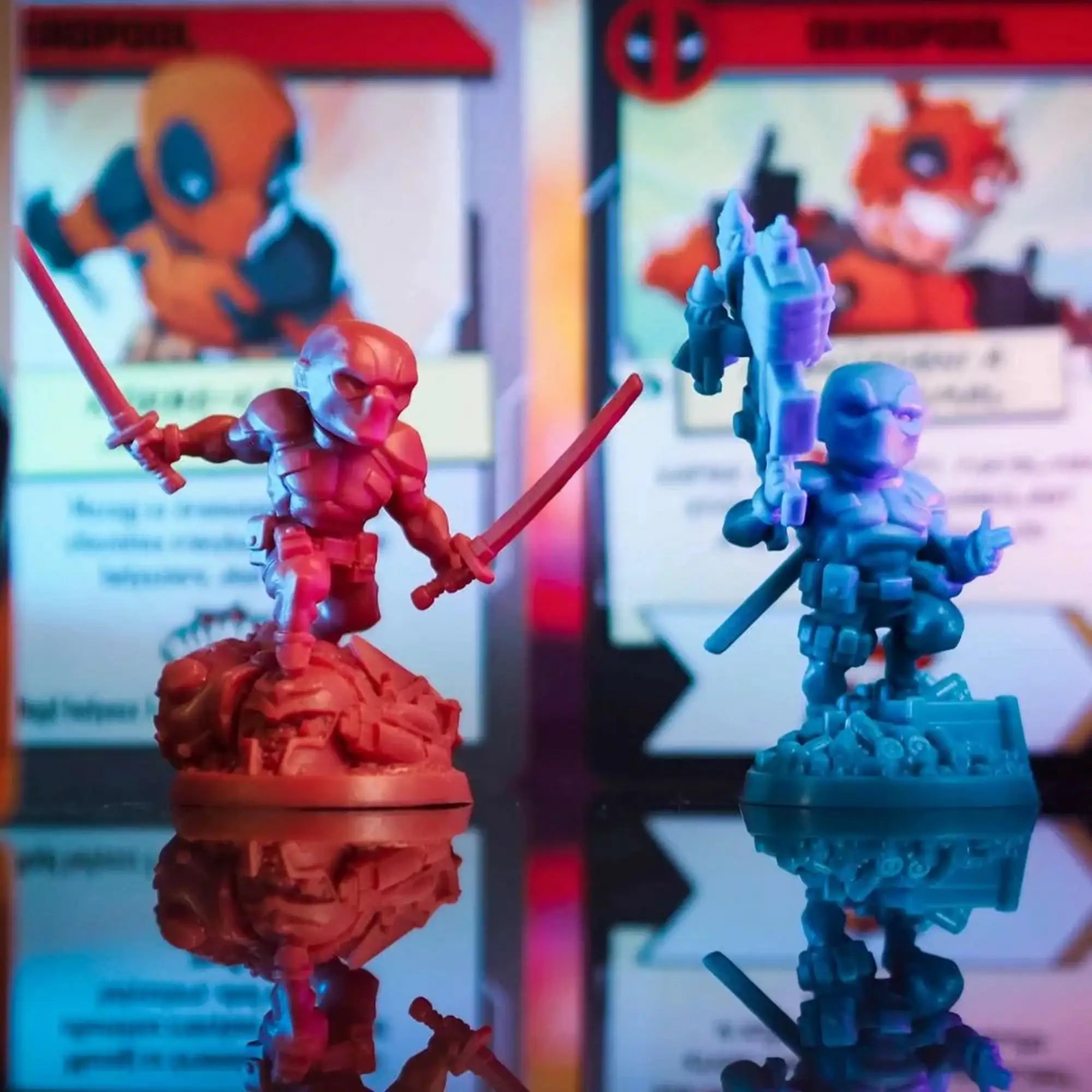 Két Deadpool figura áll az előtérben, mögöttük elmosódott karakterkártyák színes megvilágításban, kiemelve a miniatűrök részletgazdag kidolgozását.
