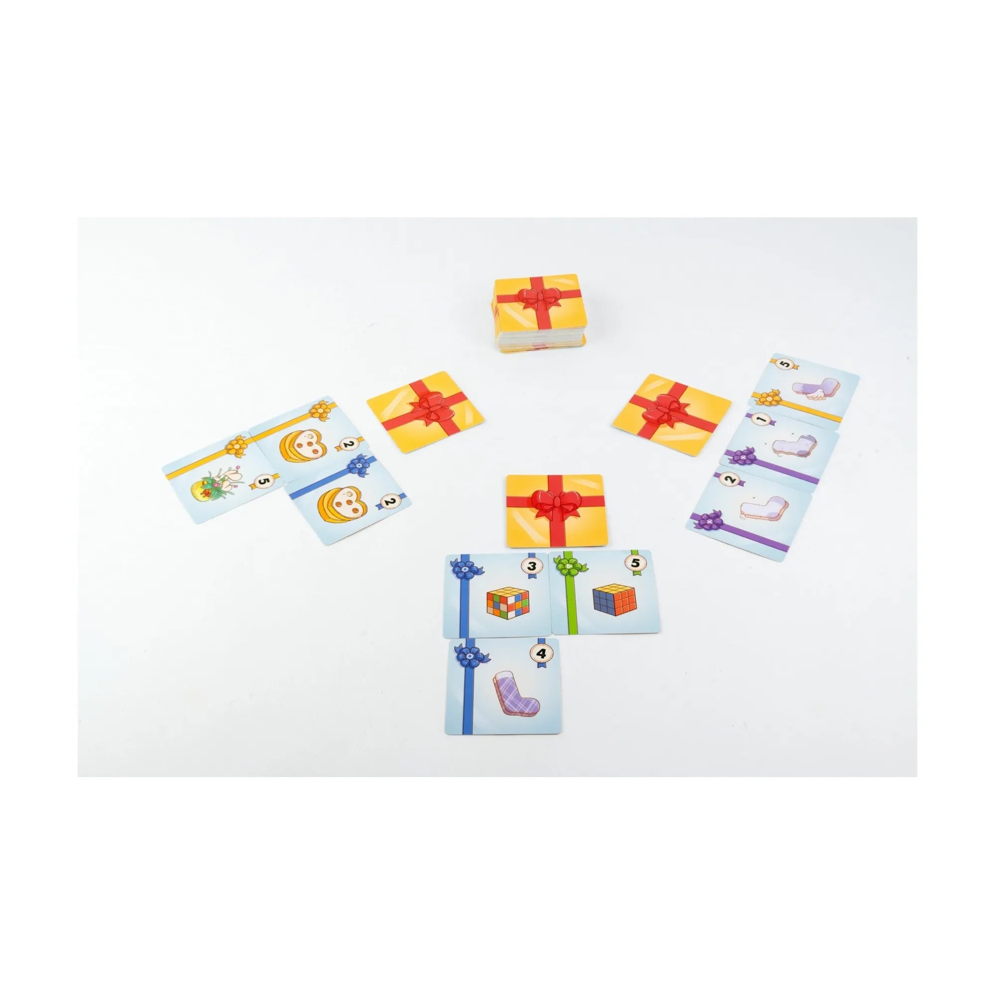 A Meglepi! társasjáték játék közben: asztalon elhelyezett ajándékkártyák és a sárga, piros szalaggal átkötött doboz.