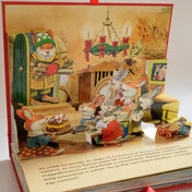 Mesél az erdő – Karácsony nyuszik karácsonya – A felnyíló oldal karácsonyi vacsorajelenetet ábrázol, ahol nyuszik ülnek az asztalnál süteménnyel és mécsesekkel.