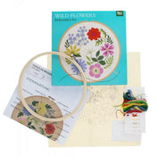 A Wild Flowers hímzőkészlet tartalma: fa hímzőkeret, előre nyomtatott virágmintás textil, színes hímzőfonalak csomagja és útmutató lapok. A háttérben a készlet doboza is látható a mintaképpel.