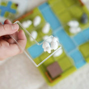 Kézben tartott átlátszó puzzle-darab két bárányfigurával a Smart Games Counting Sheep játékból.