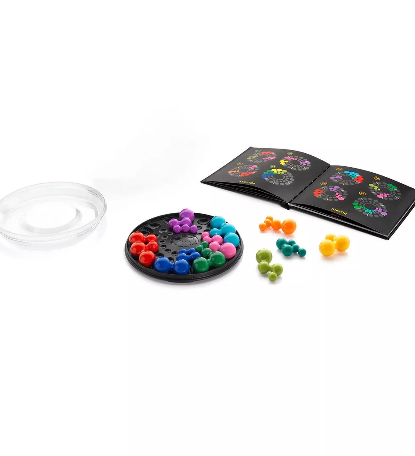 A Smart Games IQ Deluxe Circle készlet tartalma: átlátszó fedél, fekete kör alakú játéktábla, több színes műanyag puzzle-elem és egy kihívásfüzet különböző nehézségi szintekkel. A fotó bemutatja, hogyan épül fel a játék a logikai feladványok megoldása közben.