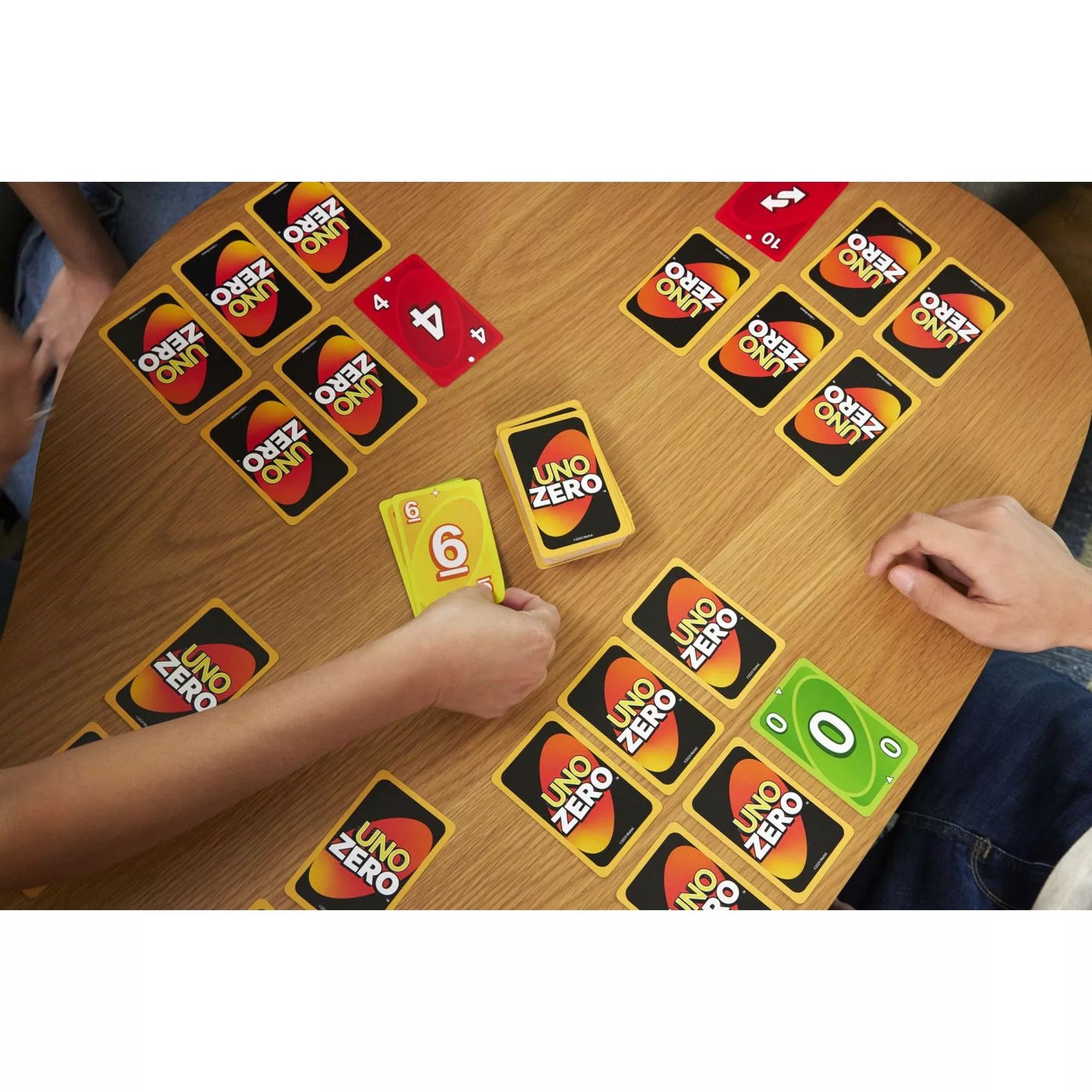 Az UNO Zero játék közbeni jelenet, ahol több játékos kártyázik egy faasztalnál. A játékosok UNO Zero hátlapú és számozott, színes kártyákkal játszanak, látható köztük sárga 6-os és zöld 0-s lap is.